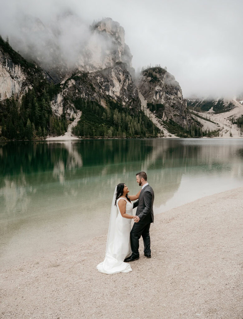 Couple in wedding attire by mountain lake.