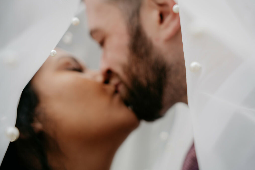 Couple kissing under a delicate veil.