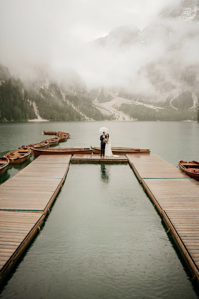 Couple under umbrella on dock with boats, foggy lake