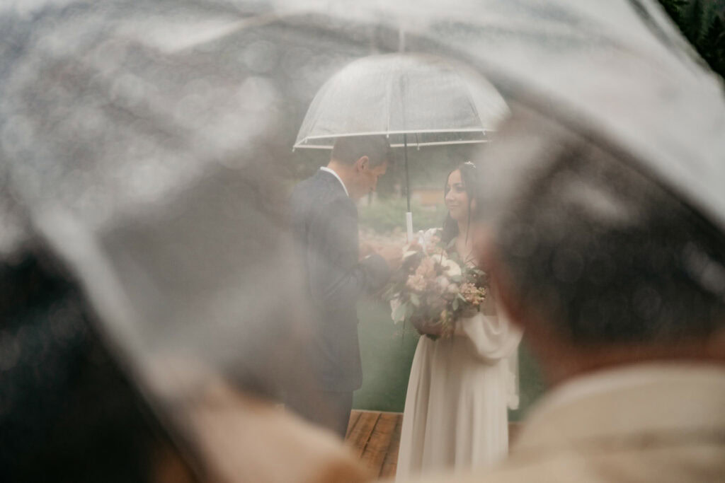 Couple exchanging vows under umbrella in rain.
