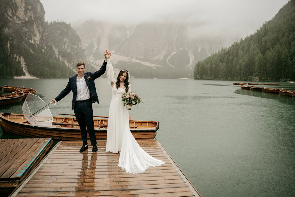 Newlyweds celebrating on rainy lakeside dock.