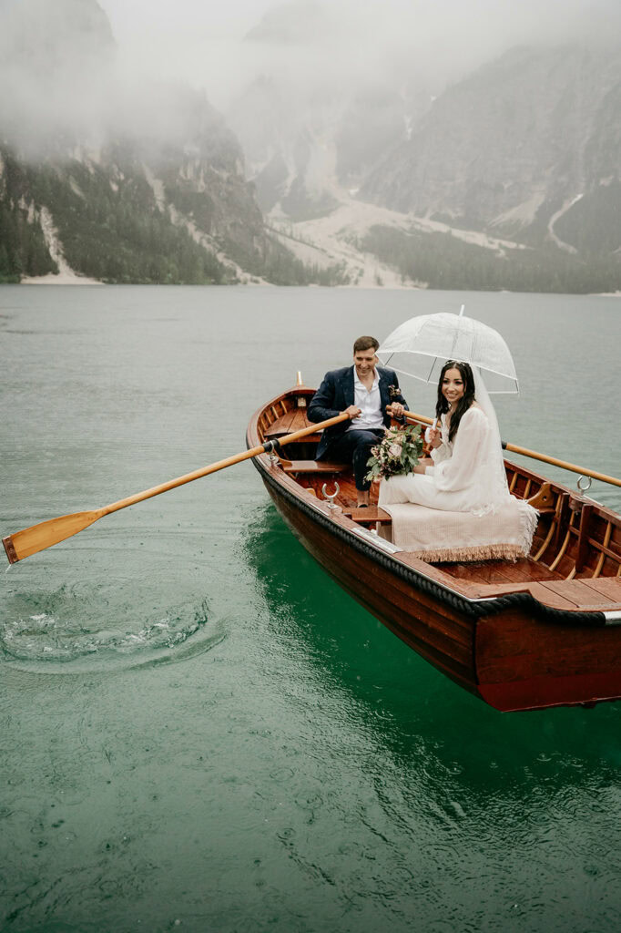Couple rowing boat on misty lake with umbrella.
