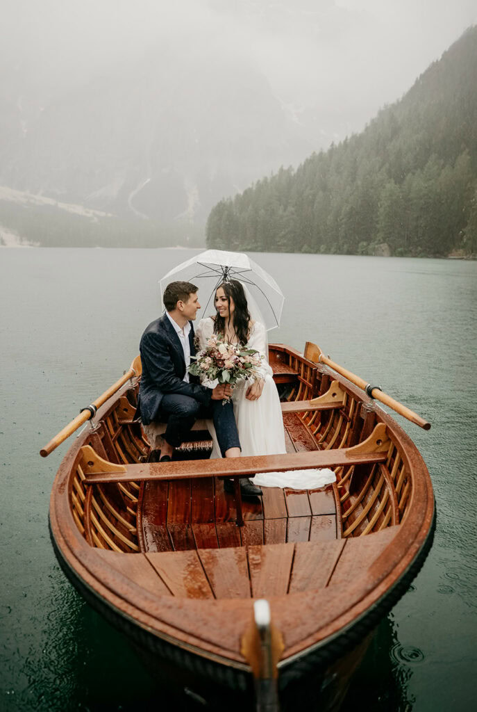 Couple under umbrella in boat on rainy lake.