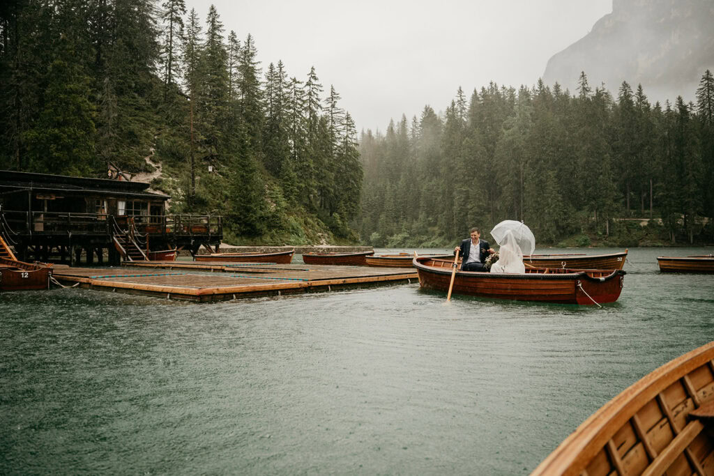 Couple rowing boat on lake under umbrella.