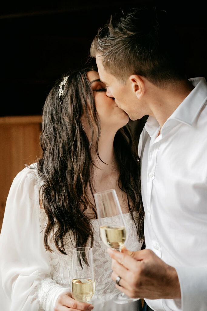 Couple kissing, holding champagne glasses, wedding celebration.