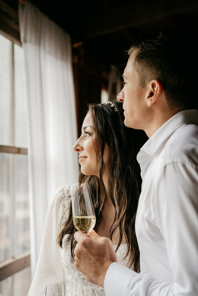 Couple gazing out window holding champagne glasses.