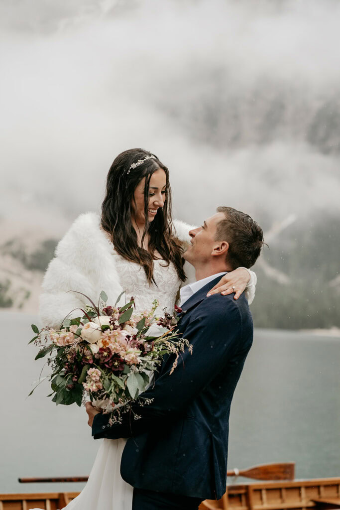 Bride and groom smiling by a misty lake.