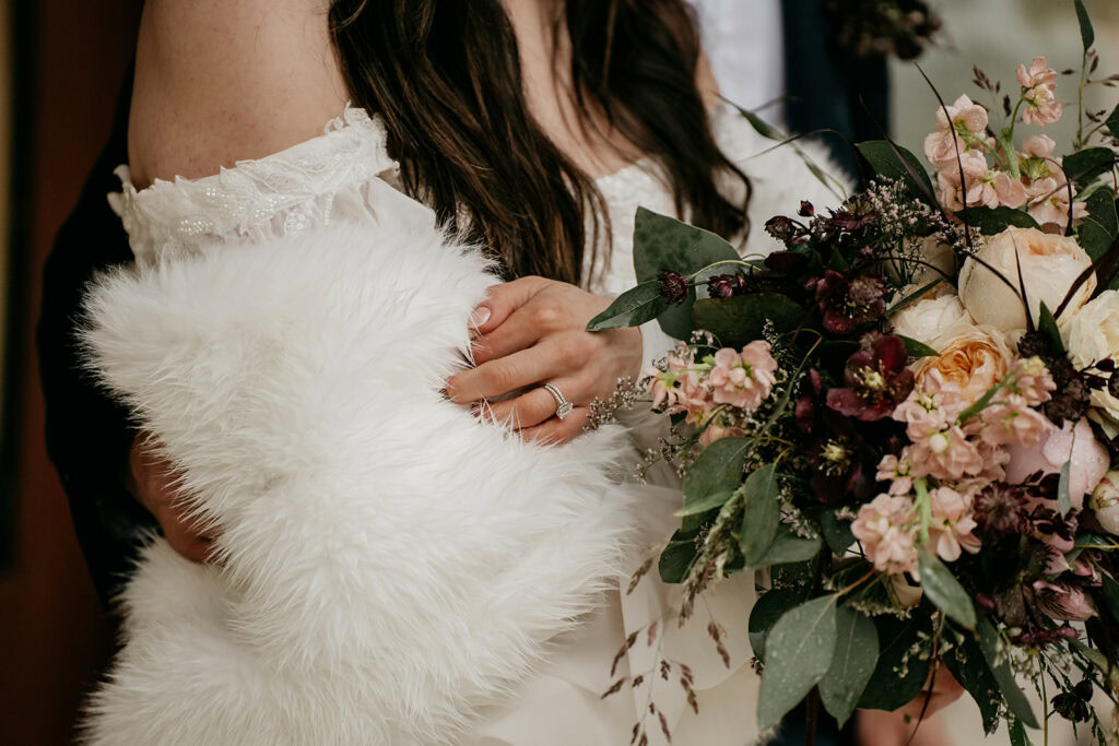 Bride holding floral bouquet with white fur wrap.
