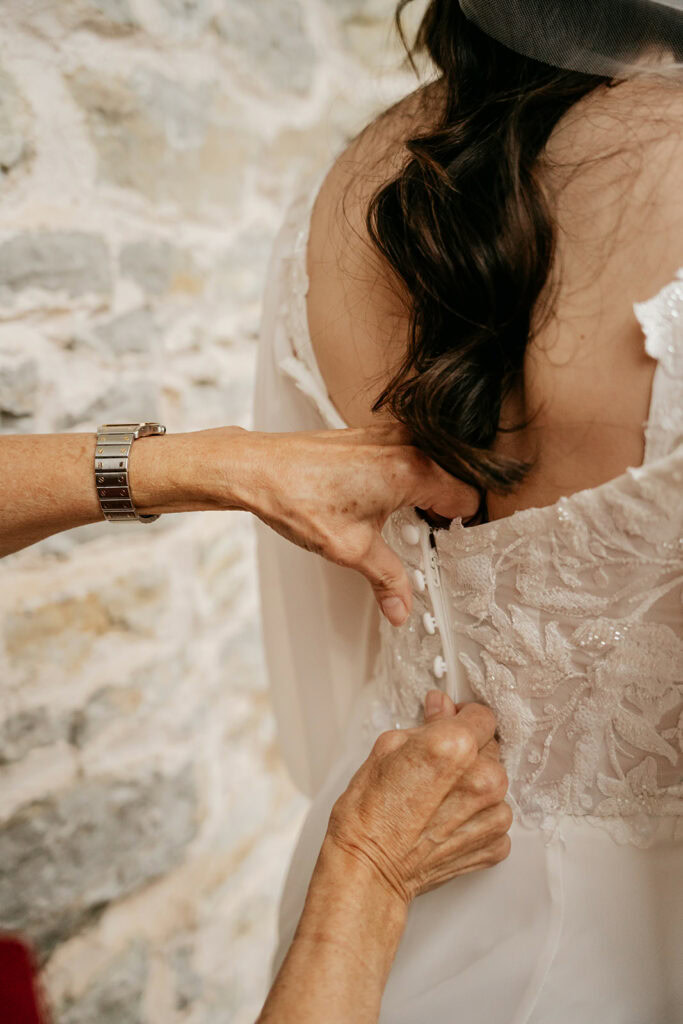 Hands buttoning wedding dress, intricate lace details.