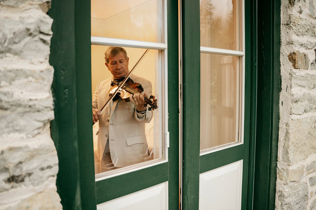 Man playing violin inside room near window.
