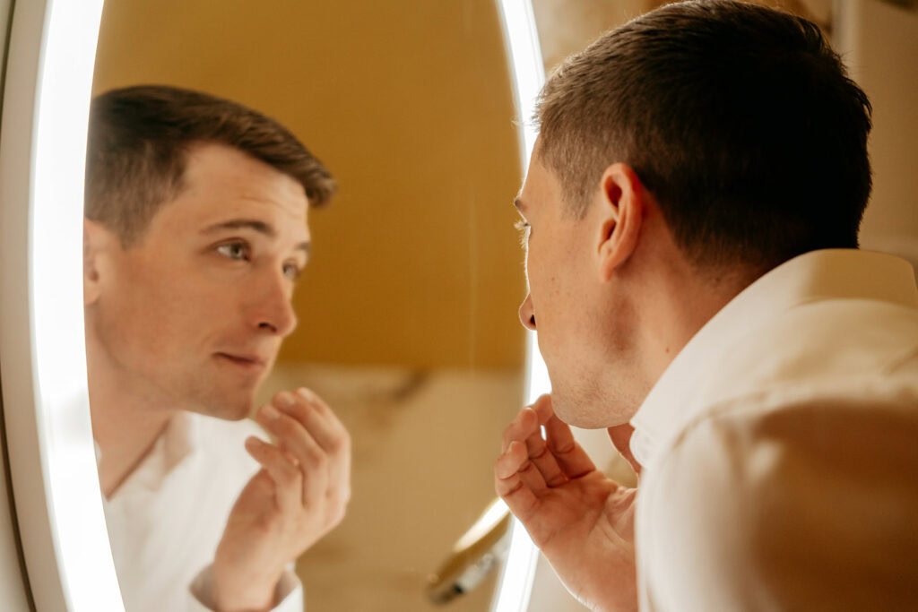 Man examining face in illuminated mirror.
