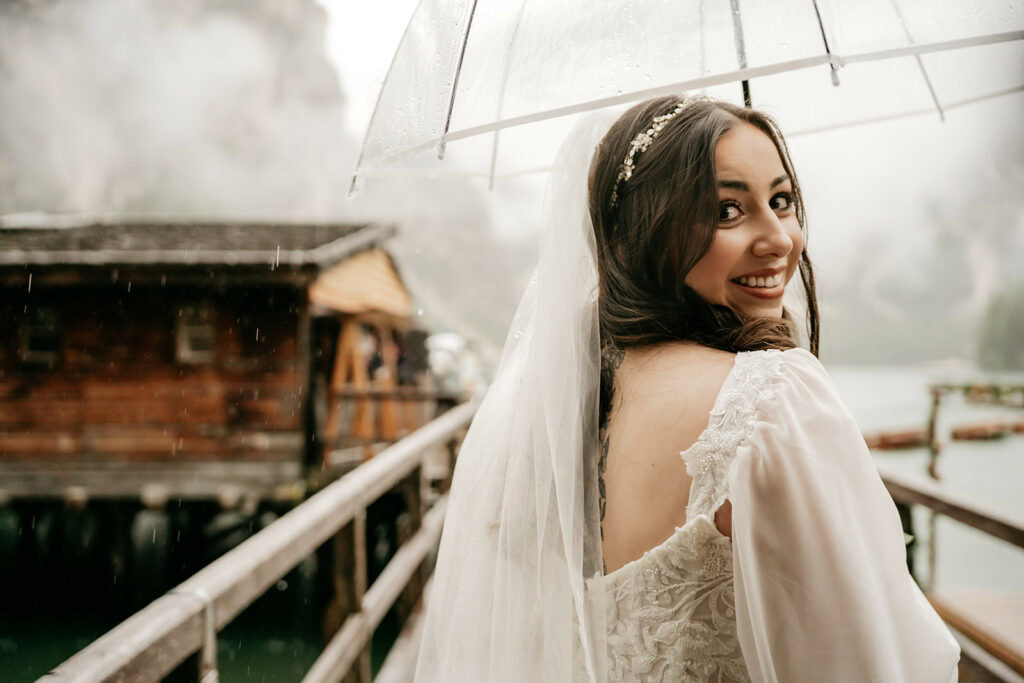 Smiling bride under umbrella, rustic background.