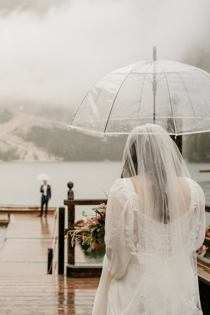 Bride on dock in rain with umbrella.