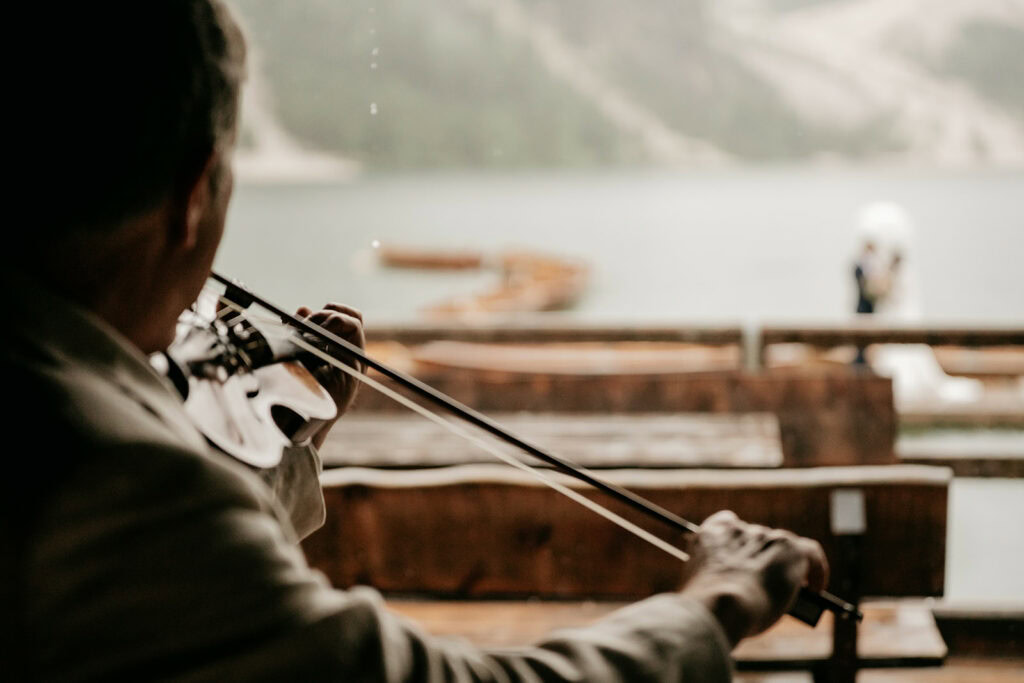 Violinist playing near lake with boats.