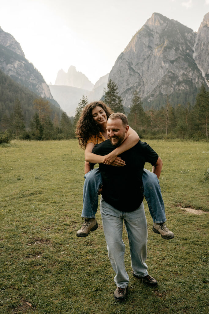 Couple piggyback in mountain meadow.
