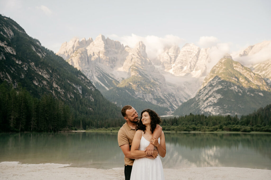 Couple embracing by mountain lake backdrop.