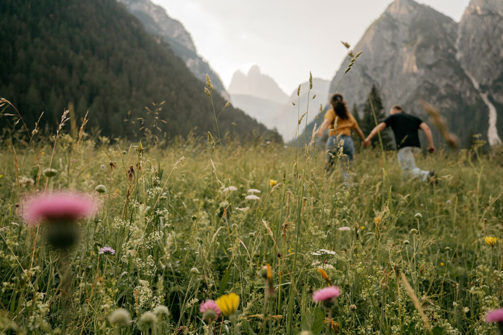 Couple running through mountain meadow at sunset.