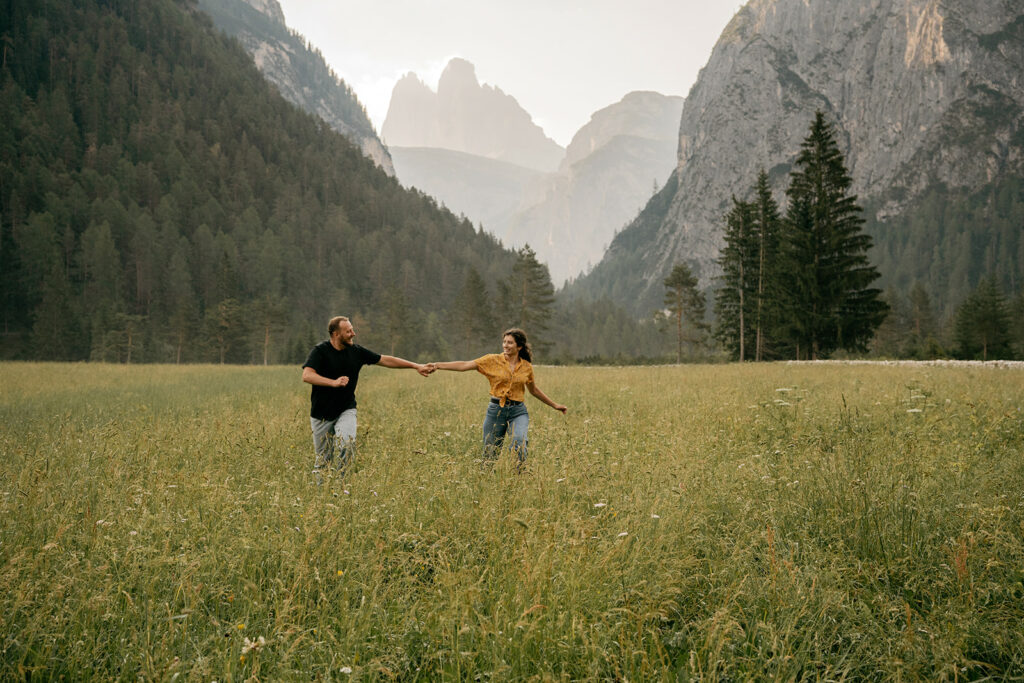 Couple running in a field with mountains.