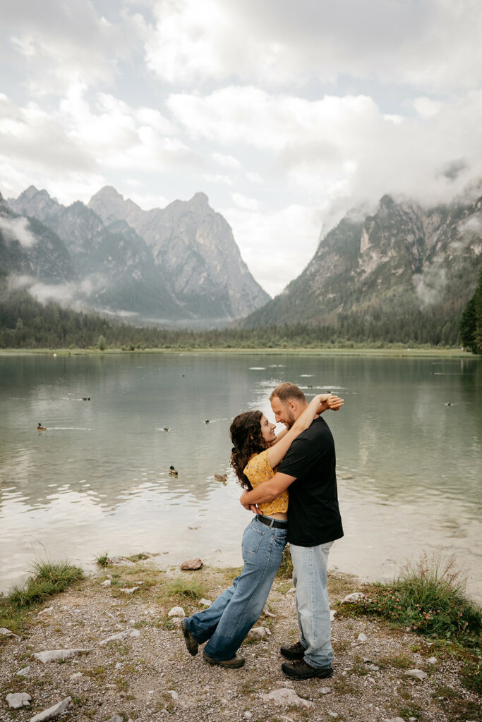 Couple embracing by mountain lake with ducks.