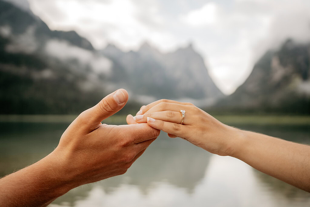 Couple holding hands with engagement ring focus.