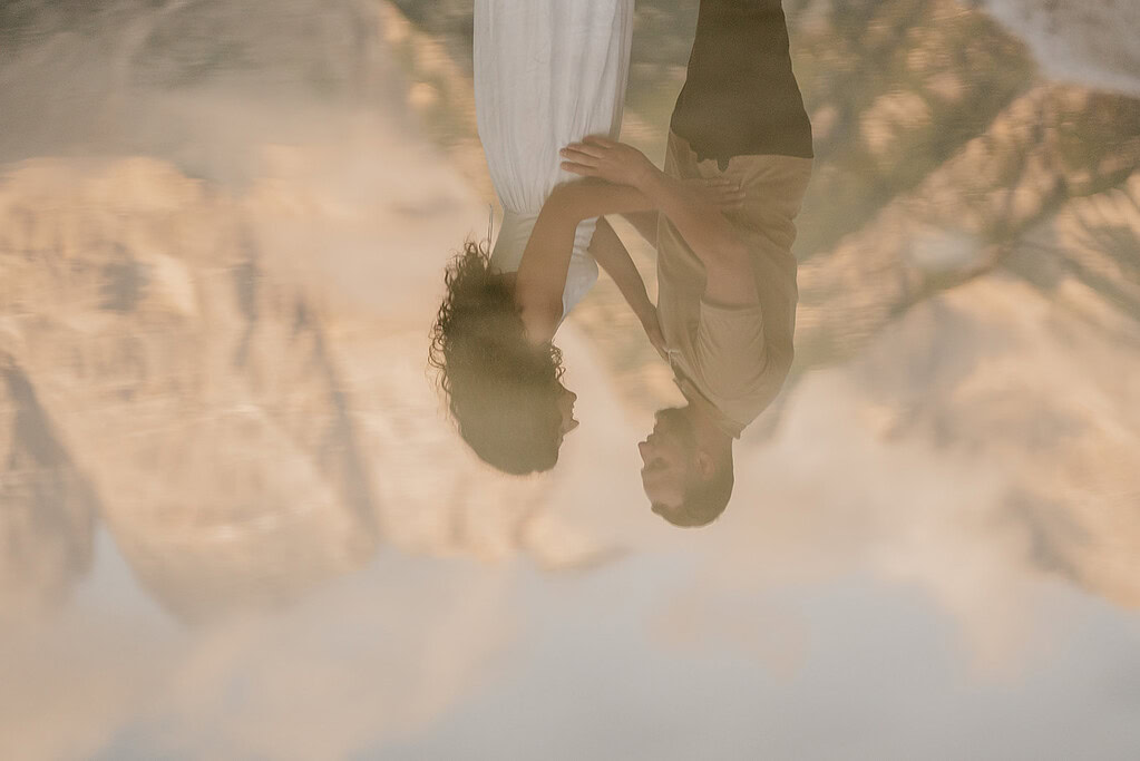 Couple reflection in serene water with mountain backdrop.