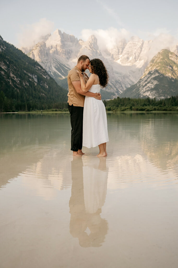 Couple embraces in serene mountain lake scenery.