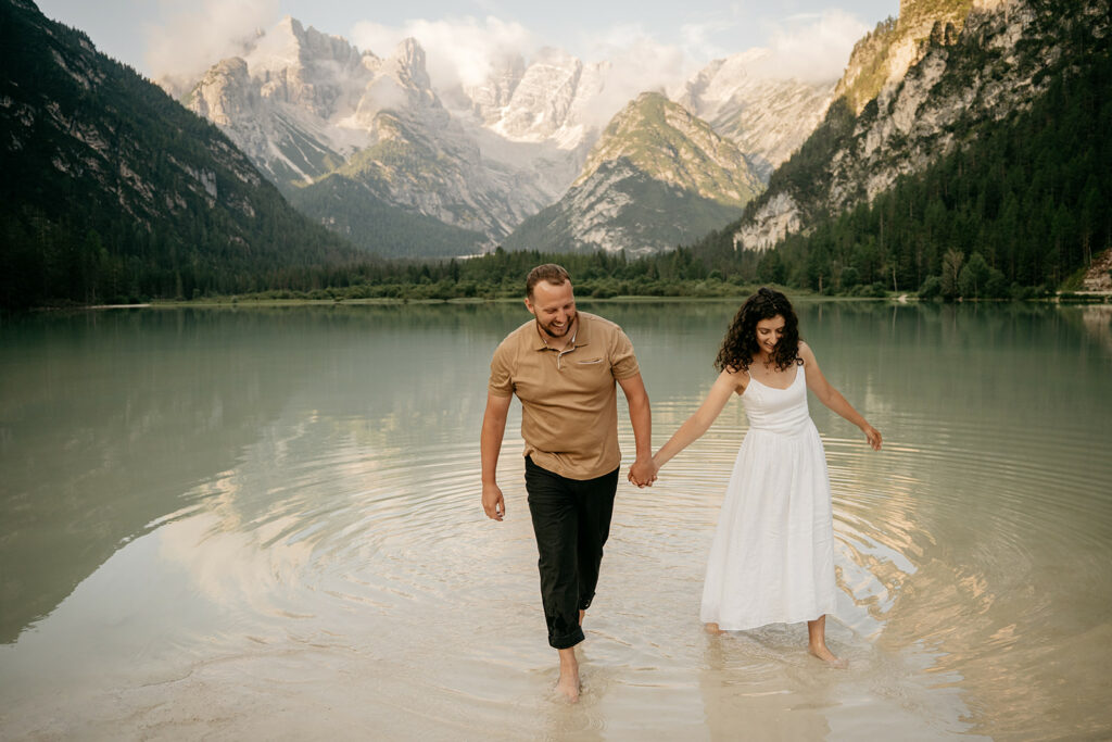 Couple walking in lake with mountain backdrop.