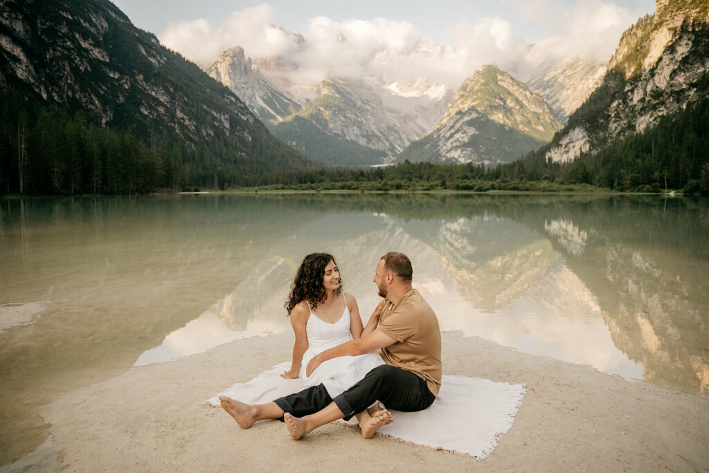 Couple sitting by mountain lake, serene landscape view.