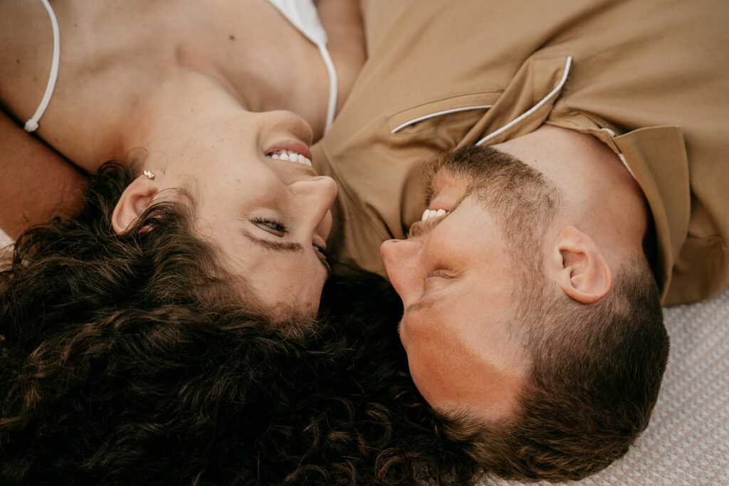 Couple smiling, heads touching, lying on blanket.