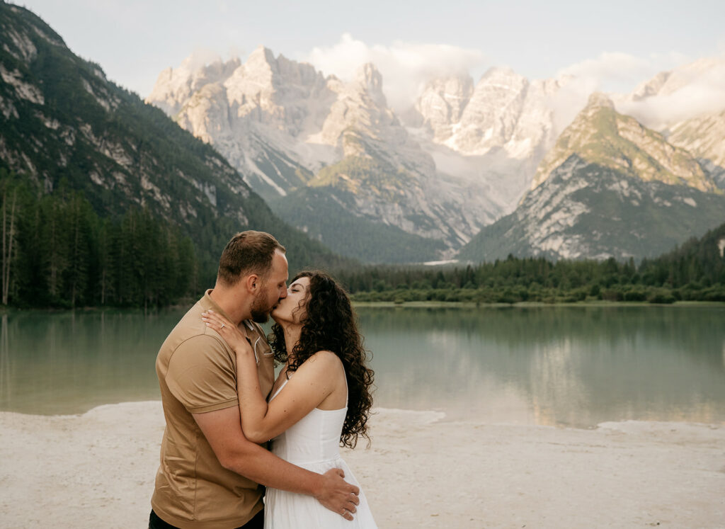 Couple kissing by mountain lake with scenic view.