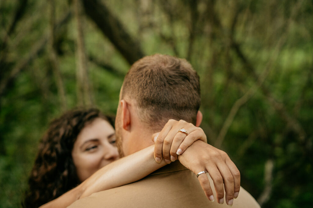 Couple embracing in nature with visible rings.