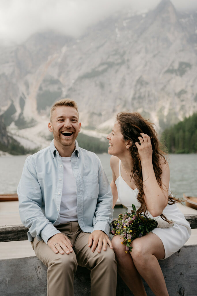 Smiling couple sitting by mountain lake.