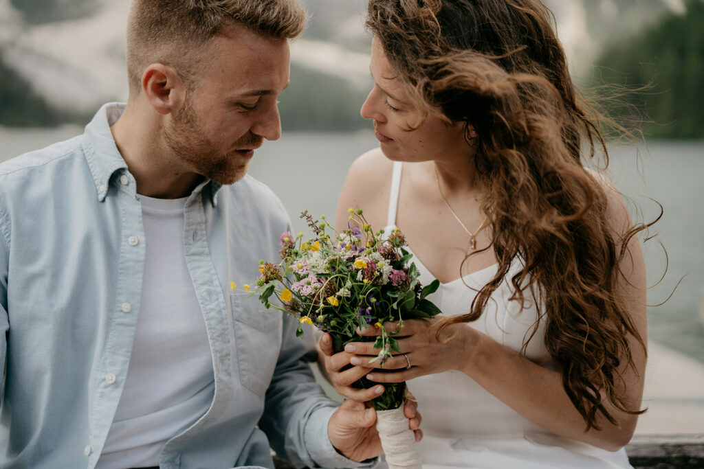 Couple holding colorful flower bouquet by a lake.