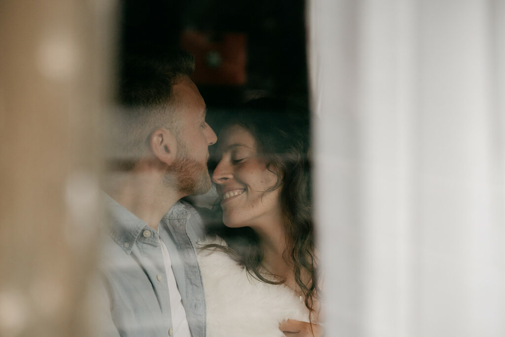 Couple smiling, cuddling behind glass window.