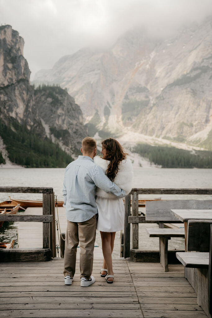 Couple embracing on lakeside dock with mountain view.