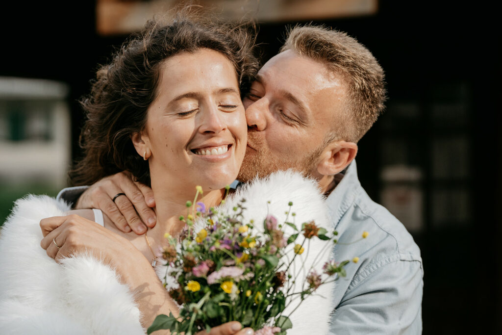 Couple embraces with bouquet, smiling and happy.