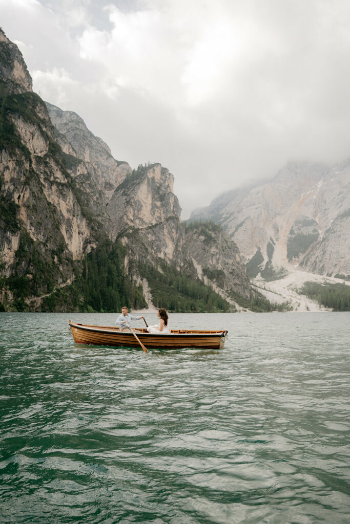 Couple rowing boat on mountain lake under clouds.