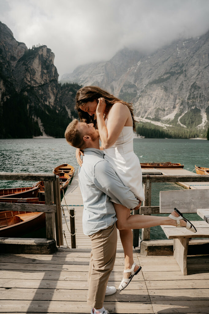 Couple embracing on dock with mountains in background.