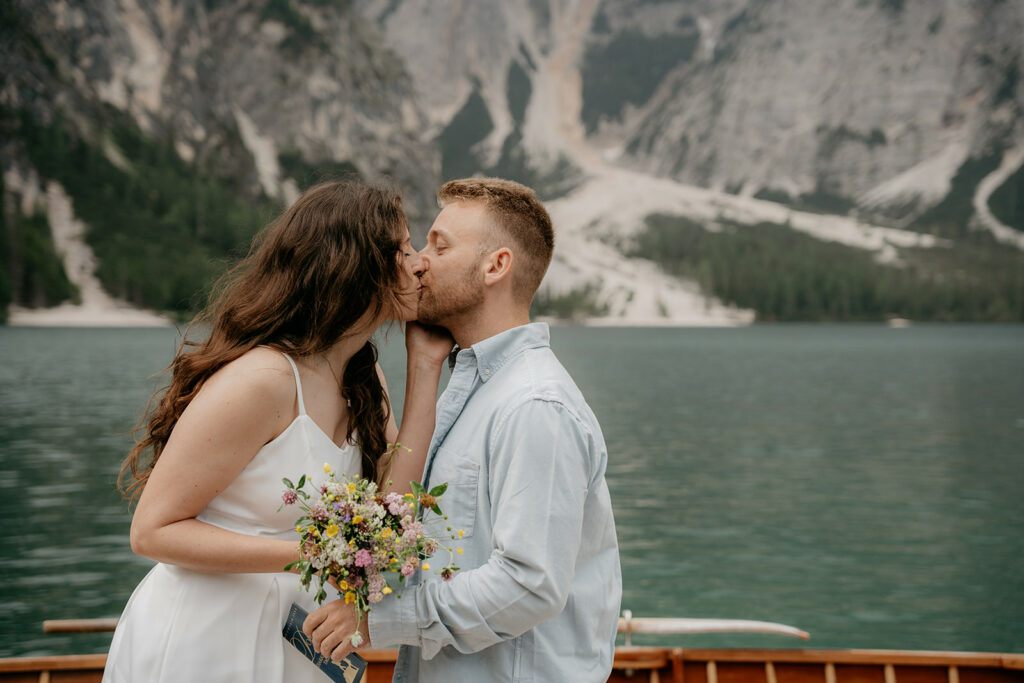 Couple kissing by lake with mountain background.