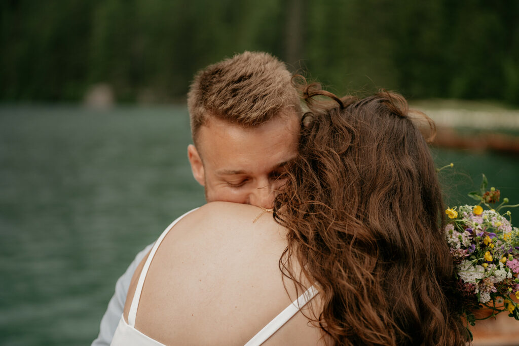 Couple embracing by a lake with flowers.