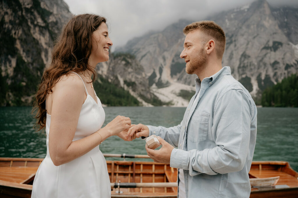 Couple engaged by mountain lake with boat.