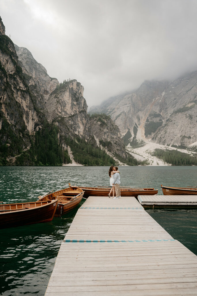 Couple embraces on dock with mountain view.