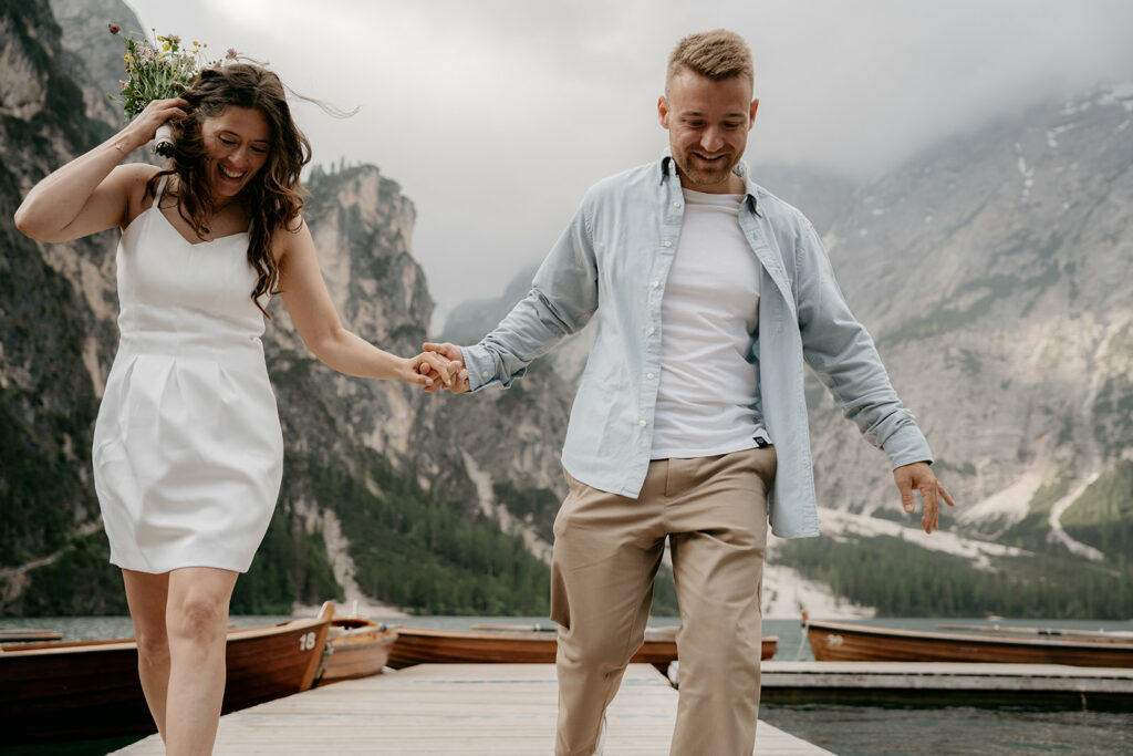 Couple holding hands walking on lakeside boardwalk.
