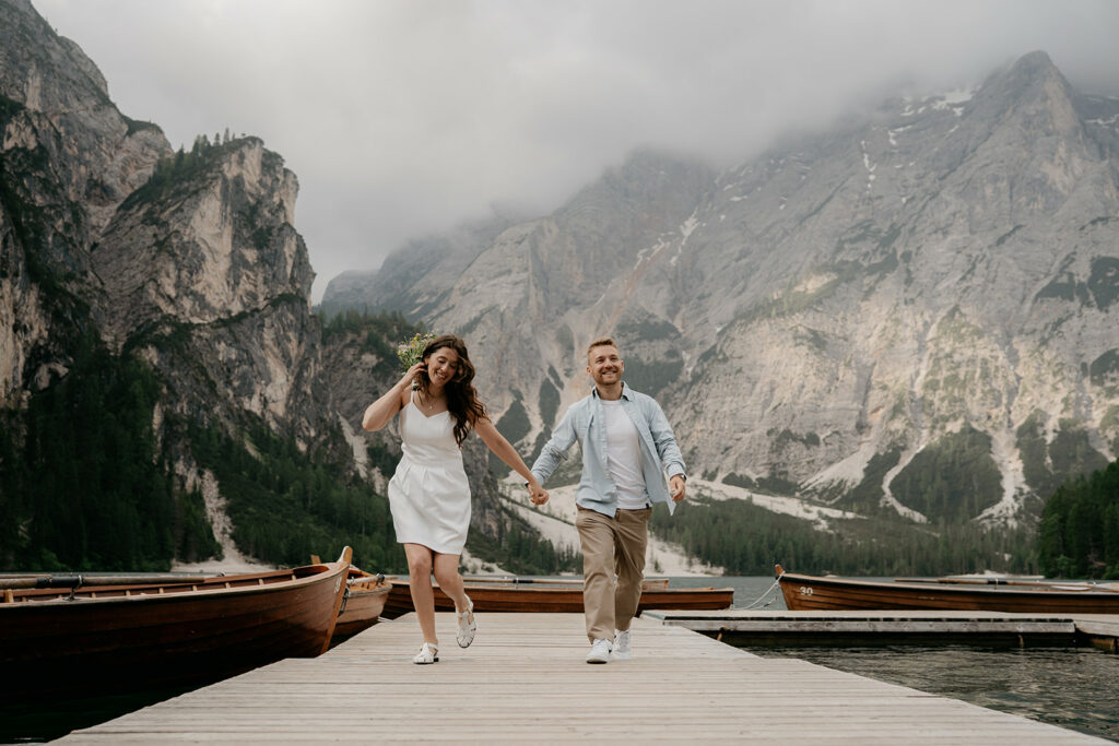 Couple smiling on dock with mountain backdrop.