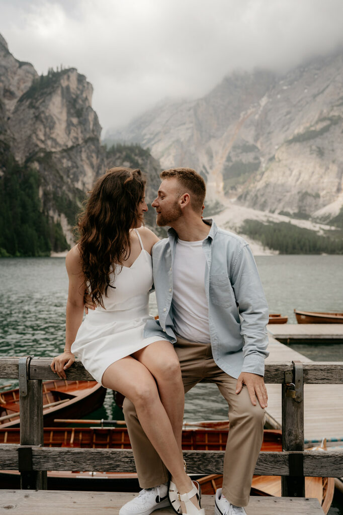 Couple sitting by lake with mountains in background.
