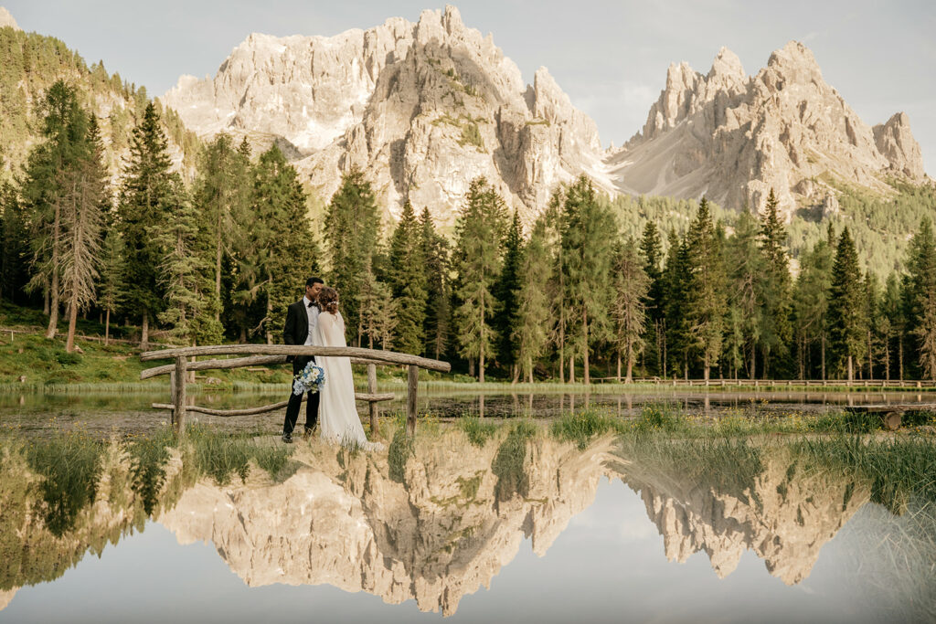 Couple embraces on bridge by scenic mountain landscape.