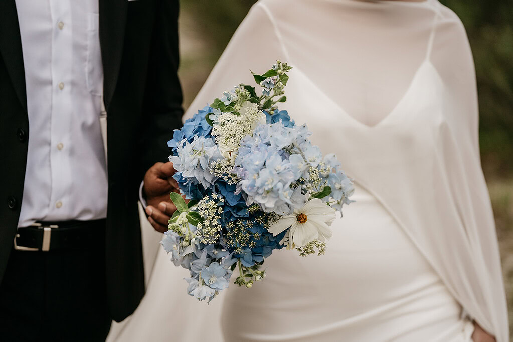 Bride holding bouquet of blue and white flowers.
