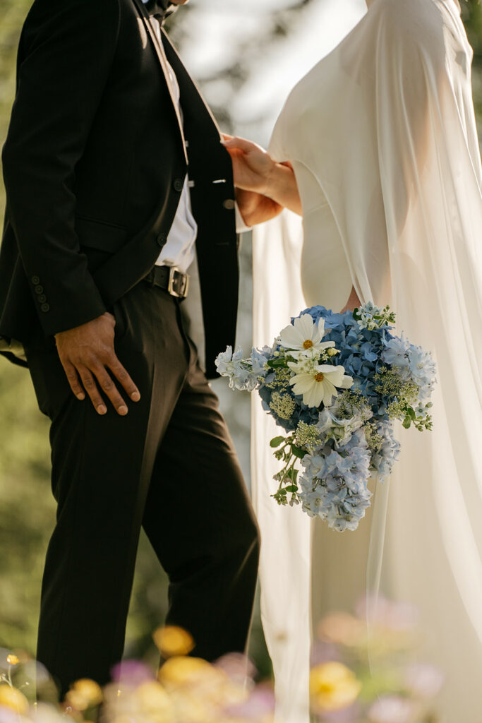 Bride holding bouquet, standing with groom outdoors.