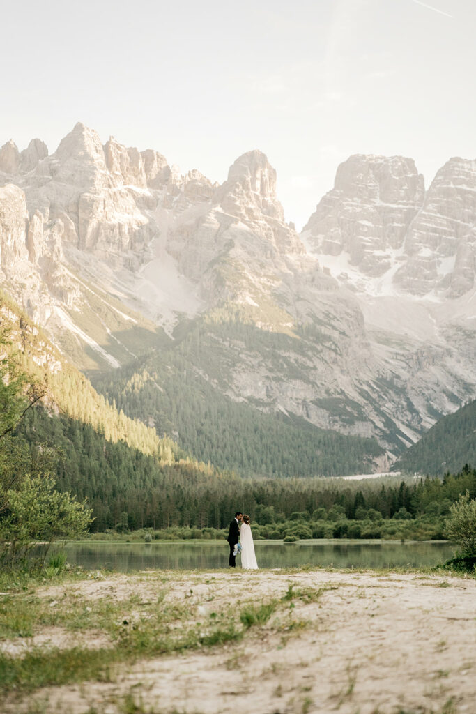 Couple in wedding attire by mountain lake scenery.