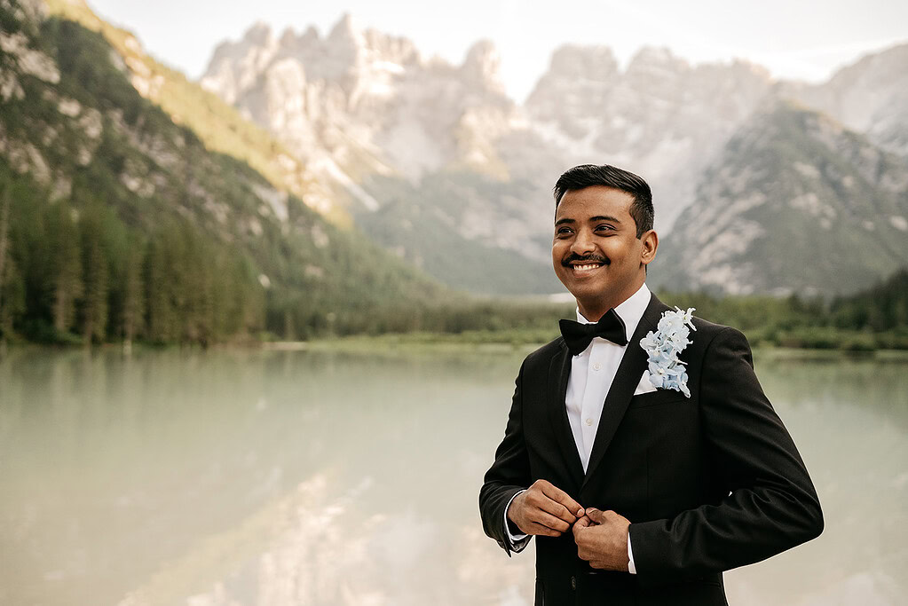 Smiling groom in tuxedo beside mountain lake.